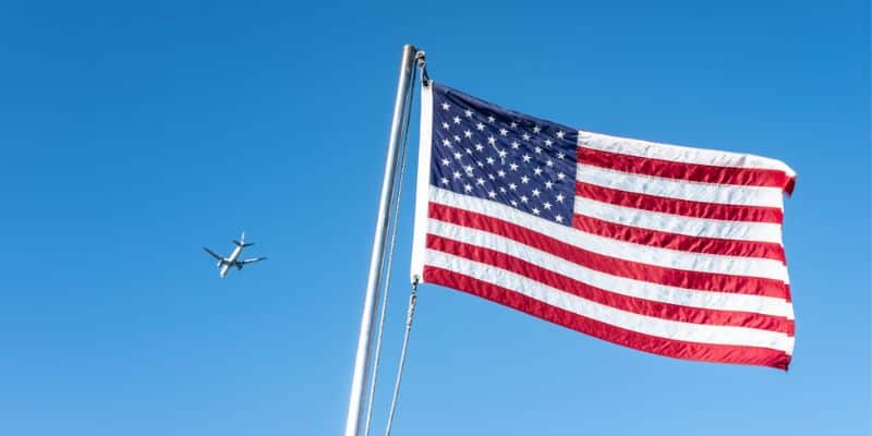 De afbeelding toont een vliegtuig op de achtergrond met de Amerikaanse vlag op de voorgrond